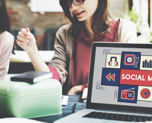 Two women working with a laptop that has the words Social Media on the screen