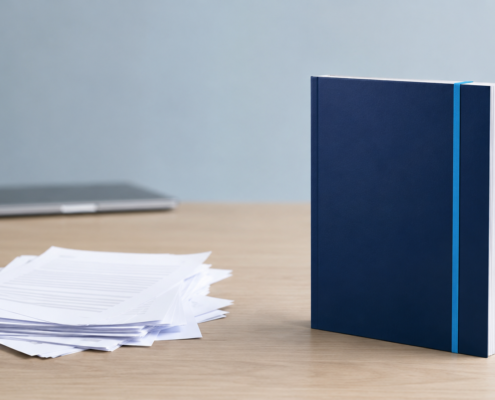 Messy stack of thin blog drafts beside one complete bound document, illustrating quality over quantity in blogging.